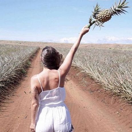 Woman holding pineapple on dirt road during Maui Pineapple Farm Tour.