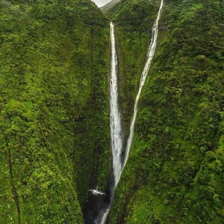 The impressive waterfall cascading down in a lush green valley during a helicopter ride in Maui.