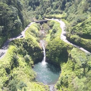 Road To Hana Gold features a scenic waterfall and road in a lush green valley in Maui.