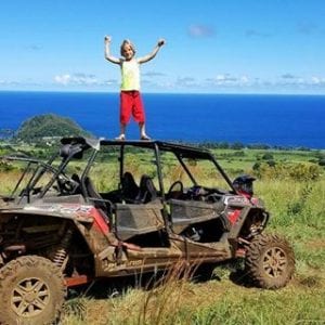 Child standing atop a dirty ATV after a Maui adventure.